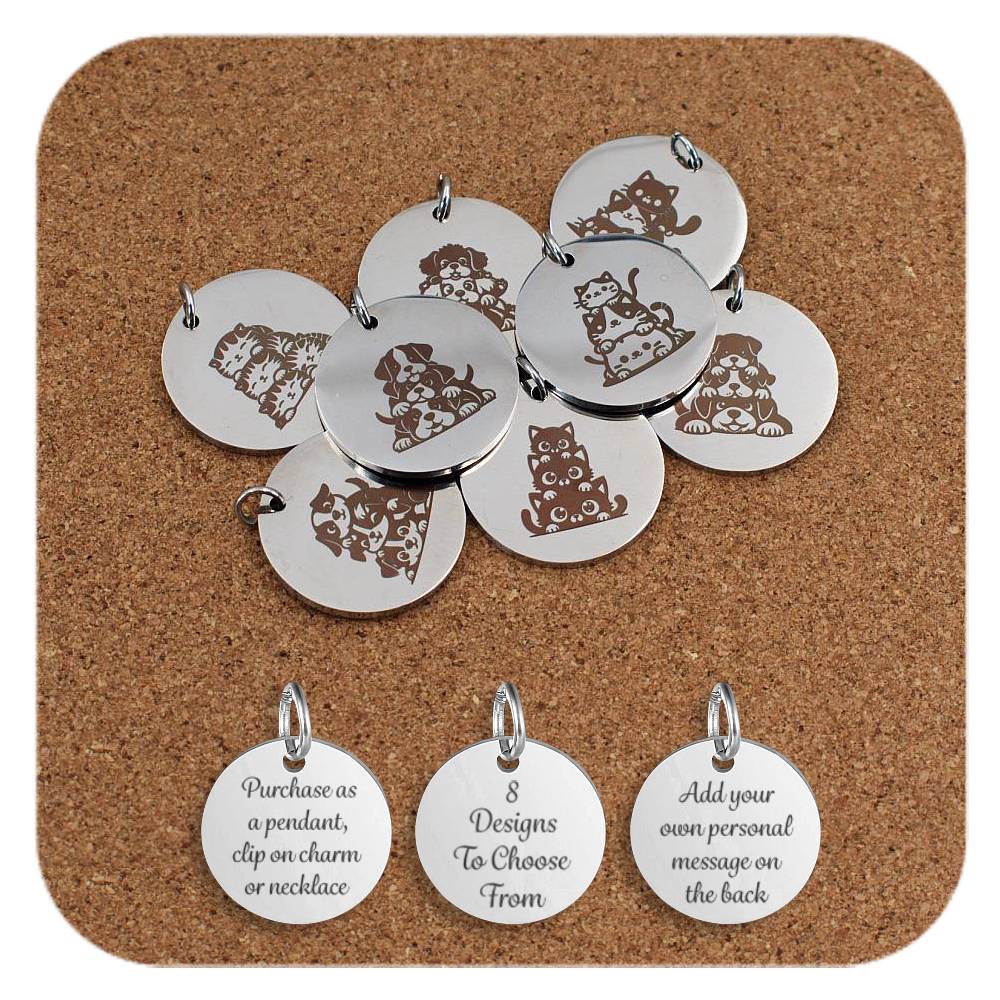 Set of round silver metal pendants engraved with various cute cat and dog designs, displayed on a cork board. Each pendant features a unique illustration such as stacked cats, playful kittens, and puppies in different poses. Below the pendants are three additional discs engraved with text that reads: 'Purchase as a pendant, clip on charm or necklace,' '8 Designs To Choose From,' and 'Add your own personal message on the back.'