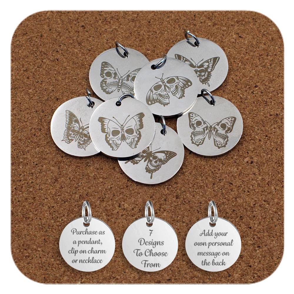 Set of round silver metal pendants engraved with various butterfly and moth designs, displayed on a cork board. Each pendant features a unique winged insect illustration, some including skull motifs or intricate wing patterns. Below the pendants are three additional discs engraved with the text: 'Purchase as a pendant, clip on charm or necklace,' '7 Designs To Choose From,' and 'Add your own personal message on the back.'