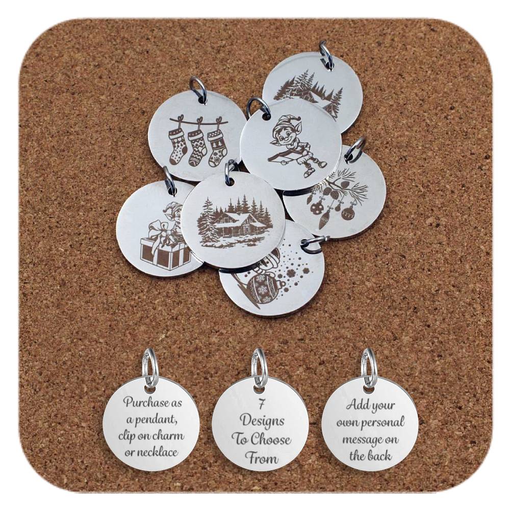 Collection of round silver metal pendants engraved with festive Christmas-themed designs, displayed on a cork board. Designs include hanging stockings, elf with list, snowy cottages, hanging baubles, elf sitting on a present, snowman and bauble. Below the pendants are three discs engraved with the text: 'Purchase as a pendant, clip on charm or necklace,' '7 Designs To Choose From,' and 'Add your own personal message on the back.'