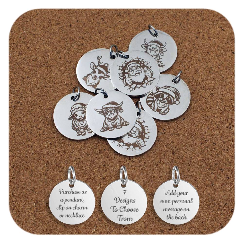 Set of round silver metal pendants engraved with festive Christmas designs, displayed on a cork board. Each pendant features a unique image including a reindeer, a raccoon in a Santa hat, a highland cow, a sheep wearing a Santa hat, and two designs showing Santa peeking through a hole in a broken wall. Below the pendants are three discs engraved with the text: 'Purchase as a pendant, clip on charm or necklace,' '7 Designs To Choose From,' and 'Add your own personal message on the back.'