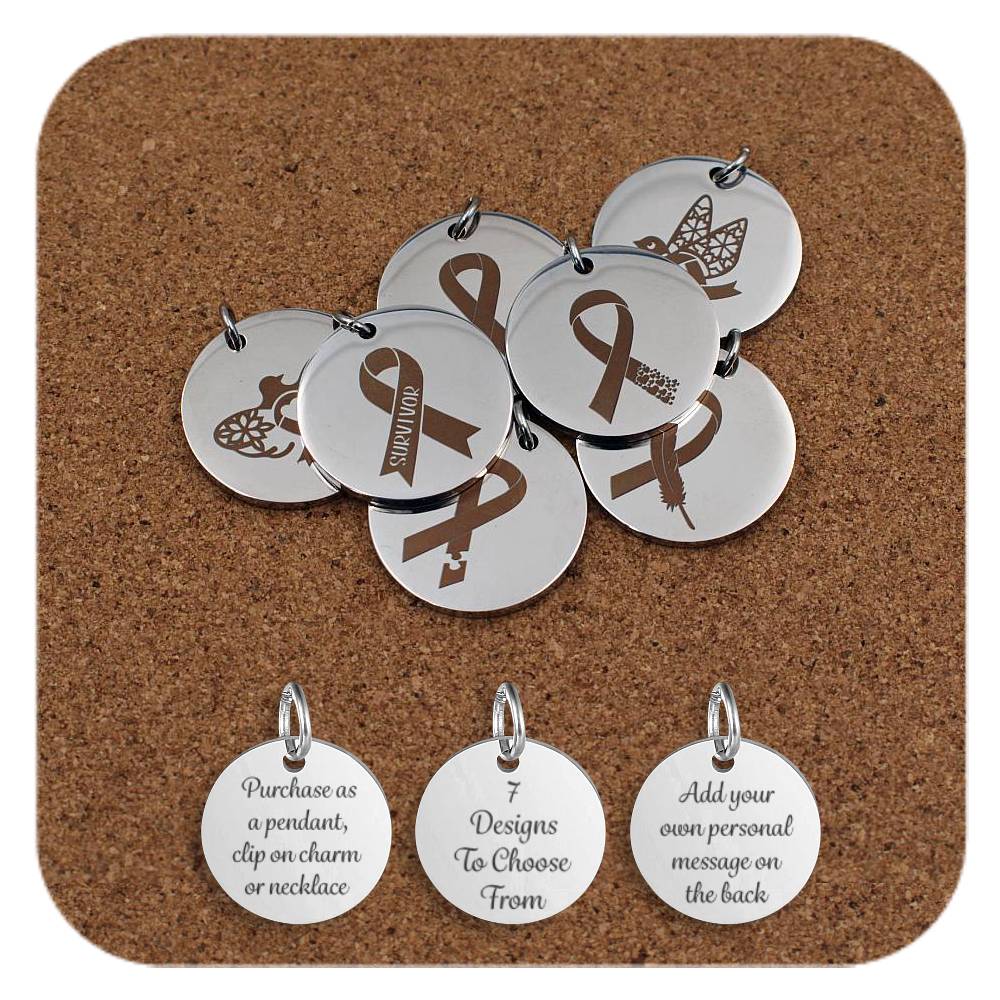 Set of round silver metal pendants engraved with various awareness ribbon designs, displayed on a cork board. Each pendant features a different ribbon illustration, including ribbons with the word 'Survivor', a key, a feather, flowers, and a butterfly. Below the pendants are three additional discs engraved with the text: 'Purchase as a pendant, clip on charm or necklace,' '7 Designs To Choose From,' and 'Add your own personal message on the back.'