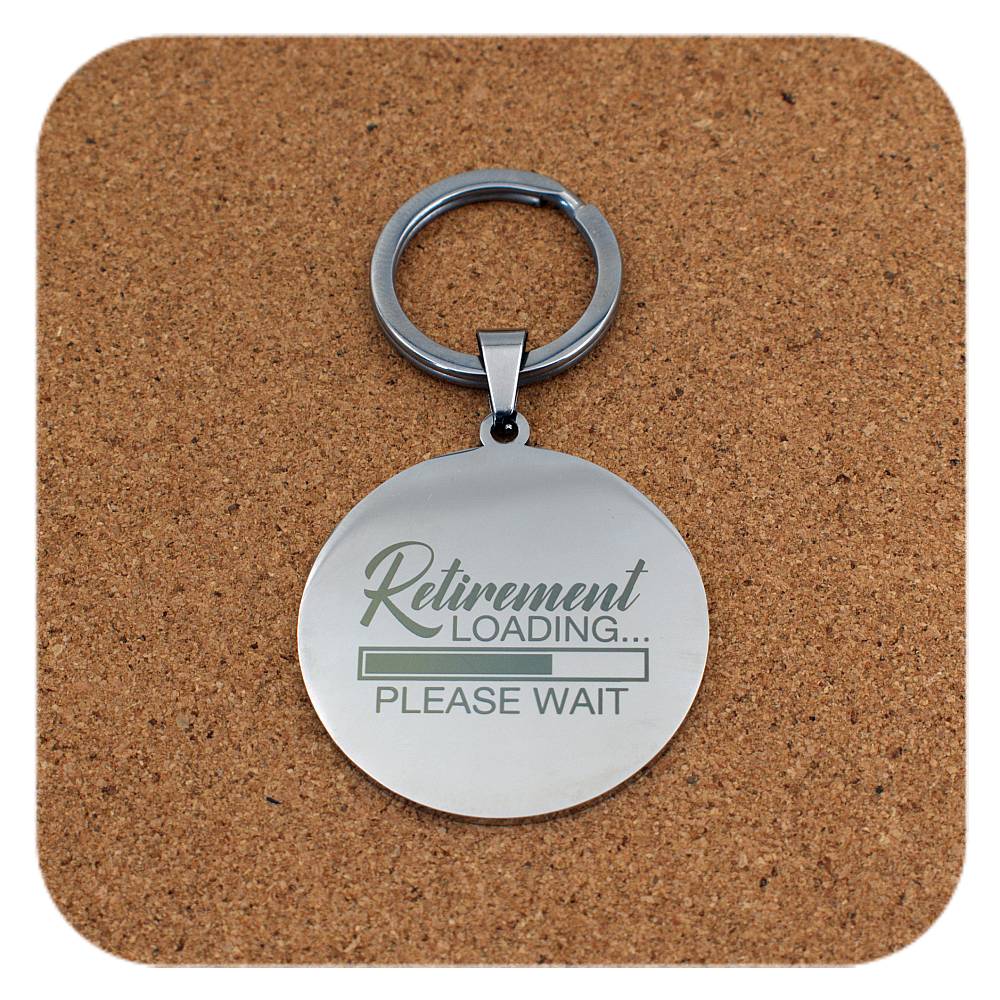 Silver keychain with 'Retirement Loading... Please Wait' text on a cork coaster