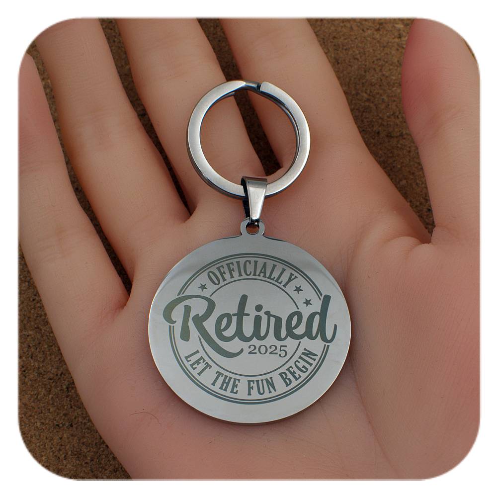 Silver keychain with 'Officially Retired 2025' text held in a hand.