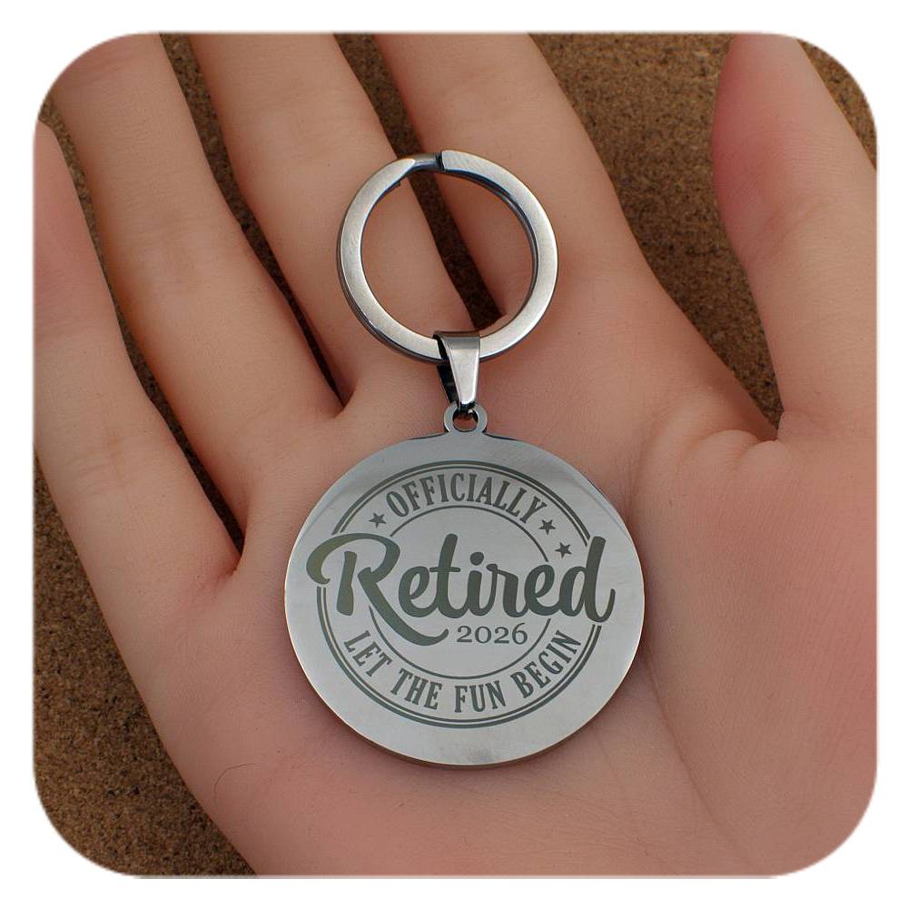Silver keychain with 'Officially Retired 2026' text held in a hand.
