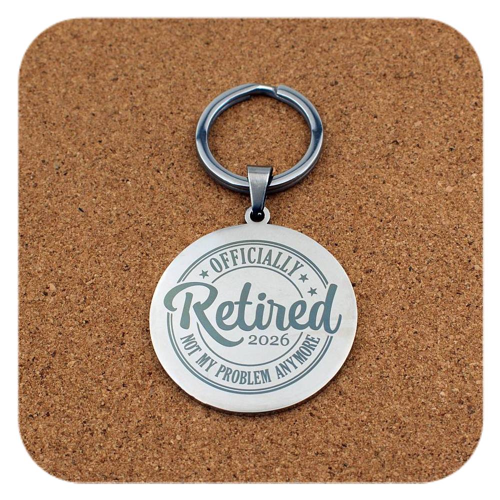 Keychain with 'Officially Retired 2026 Not My Problem Anymore' text on a cork background