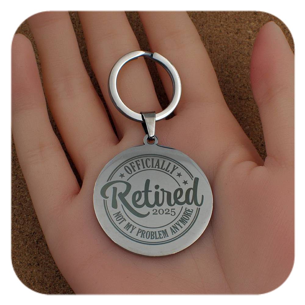 Silver keychain with 'Officially Retired 2025' text held in a hand.