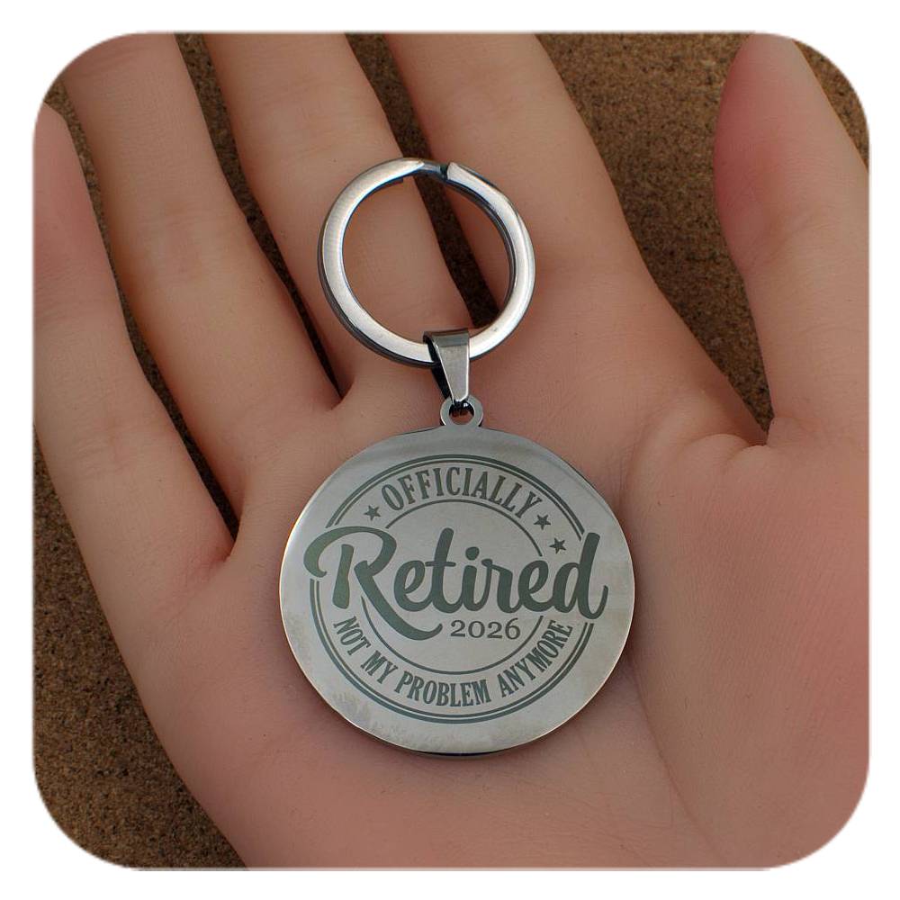 Silver keychain with 'Officially Retired 2026 Not My Problem Anymore' text held in a hand.