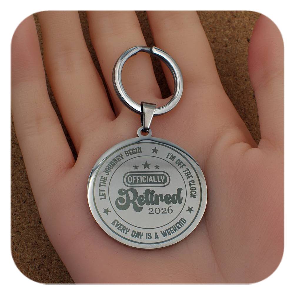 Silver keychain with 'OFFICIALLY Retired 2026' text held in a hand.