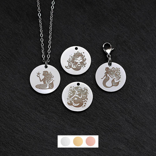 Four silver round disc pendants on a black slate background showing four different mermaid designs. One has a silver necklace attached by a jump ring and another has a lobster clasp and split ring attached to it