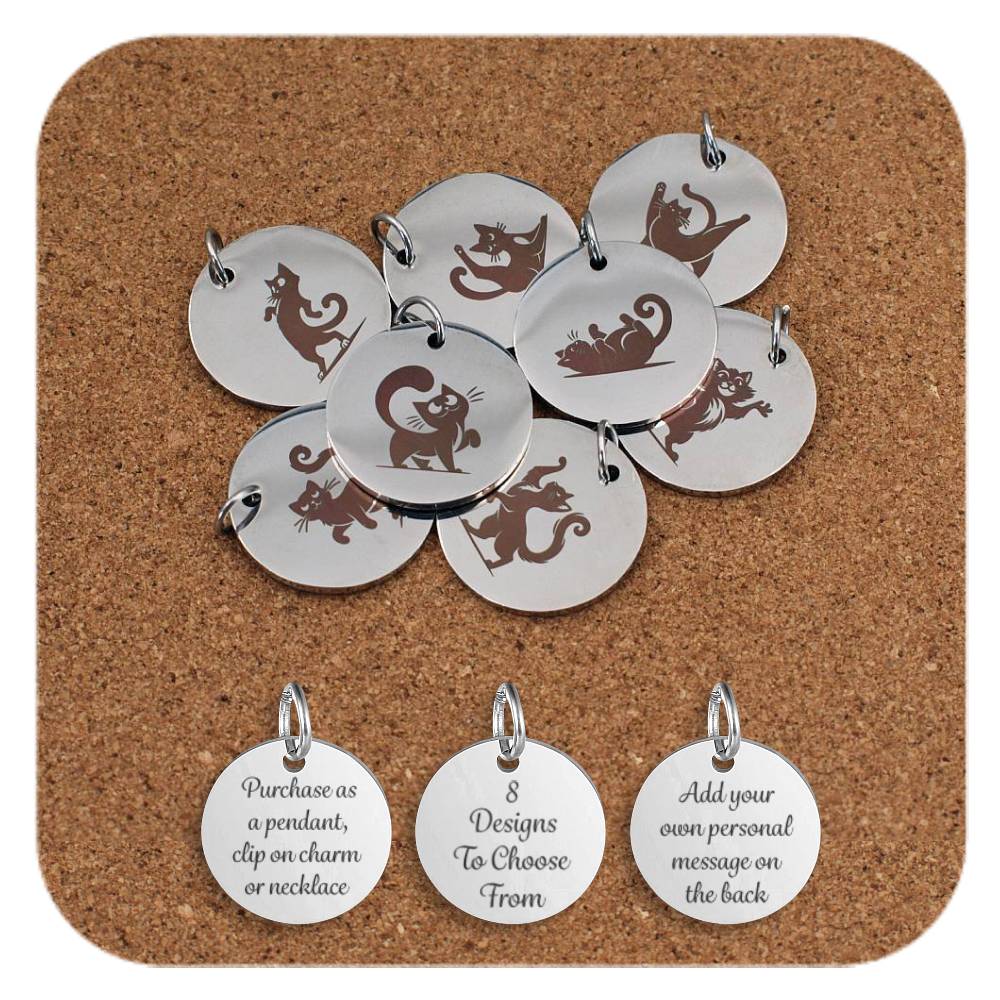 A selection of round stainless steel pendants engraved with playful cartoon cat designs, each featuring a different cat pose or activity, displayed on a cork background. Below the pendants are three additional discs showing engraved text that reads: 'Purchase as a pendant, clip on charm or necklace,' '8 Designs To Choose From,' and 'Add your own personal message on the back'