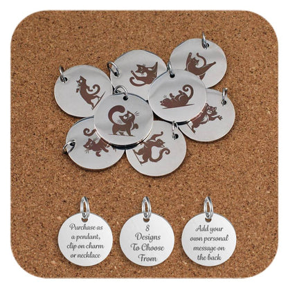 A selection of round stainless steel pendants engraved with playful cartoon cat designs, each featuring a different cat pose or activity, displayed on a cork background. Below the pendants are three additional discs showing engraved text that reads: 'Purchase as a pendant, clip on charm or necklace,' '8 Designs To Choose From,' and 'Add your own personal message on the back'