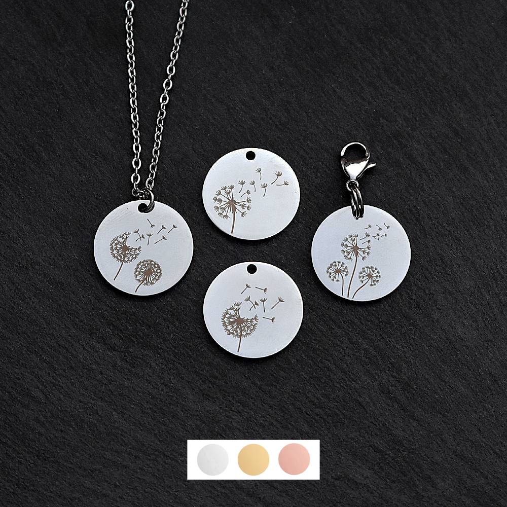 Four silver round disc pendants on a black slate background showing four different dandelion designs. One has a silver necklace attached by a jump ring and another has a lobster clasp and split ring attached to it