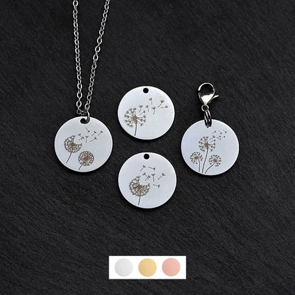 Four silver round disc pendants on a black slate background showing four different dandelion designs. One has a silver necklace attached by a jump ring and another has a lobster clasp and split ring attached to it