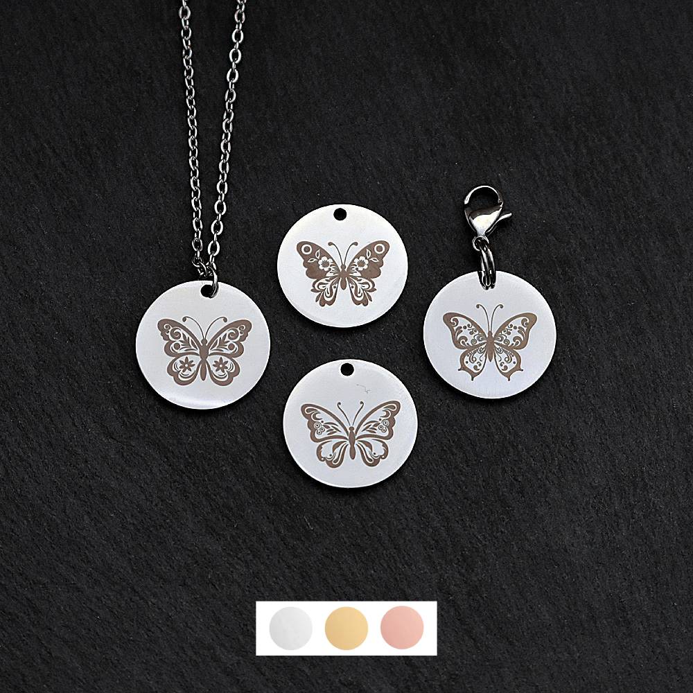 Four silver round disc pendants on a black slate background showing four different butterfly designs. One has a silver necklace attached by a jump ring and another has a lobster clasp and split ring attached to it