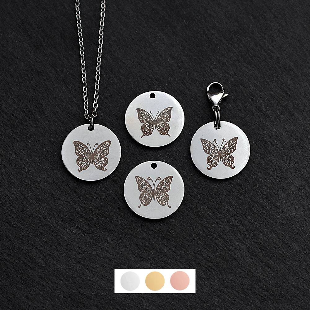 Four silver round disc pendants on a black slate background showing four different butterfly designs. One has a silver necklace attached by a jump ring and another has a lobster clasp and split ring attached to it