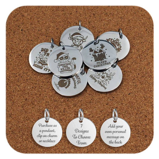 A variety of stainless steel pendants engraved with humorous and festive Christmas designs, including cartoon animals, witty text, and holiday-themed illustrations, arranged on a cork background. Below the pendants are three additional discs showing engraved text that reads: 'Purchase as a pendant, clip on charm or necklace,' '7 Designs To Choose From,' and 'Add your own personal message on the back'