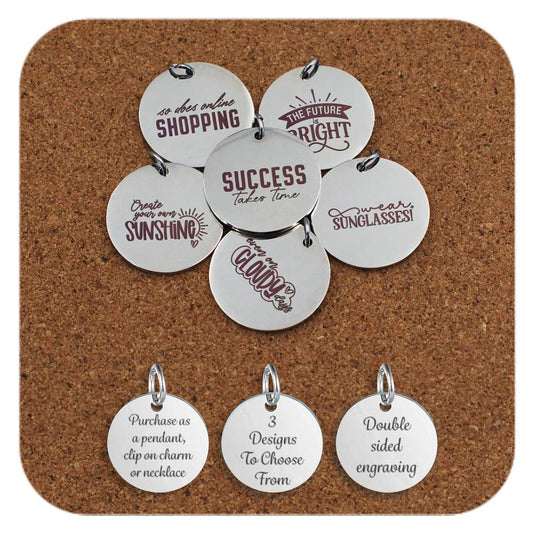 Stainless steel round pendants engraved with uplifting and humorous quotes such as 'Success takes time', 'So does online shopping', 'The future is bright', 'Create your own sunshine', and 'Even on cloudy days'. Arranged on a corkboard background with three additional tags at the bottom reading: 'Purchase as a pendant, clip on charm or necklace', '3 Designs To Choose From', and 'Double sided engraving'.