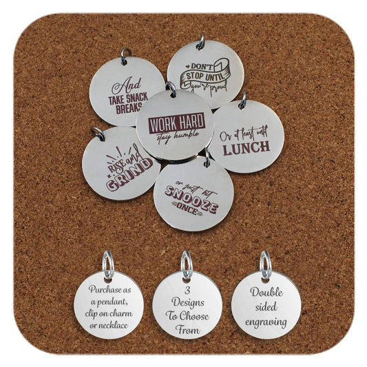 Set of engraved stainless steel pendants arranged on corkboard, each with humorous motivational phrases such as 'Work hard stay humble', 'Don’t stop until you’re proud', 'And take snack breaks', 'Rise & grind', 'Or at least until lunch', and 'Or hit snooze once'. Below, three tags read: 'Purchase as a pendant, clip on charm or necklace', '3 Designs To Choose From', and 'Double sided engraving'.