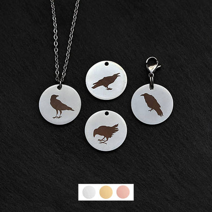 Four silver round disc pendants on a black slate background showing four different black raven rook birds. One has a silver necklace attached by a jump ring and another has a lobster clasp and split ring attached to it