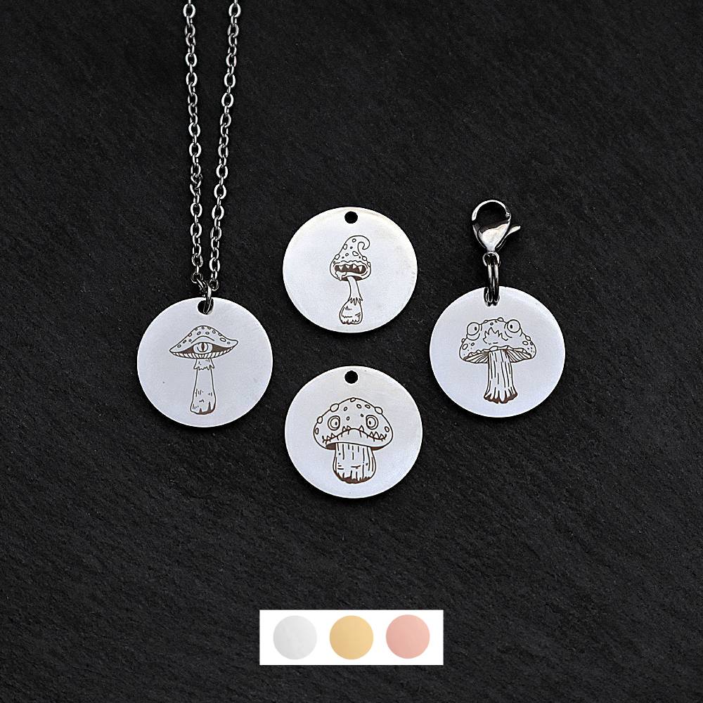 Four silver round disc pendants on a black slate background showing four different creepy mushroom toadstool designs. One has a silver necklace attached by a jump ring and another has a lobster clasp and split ring attached to it