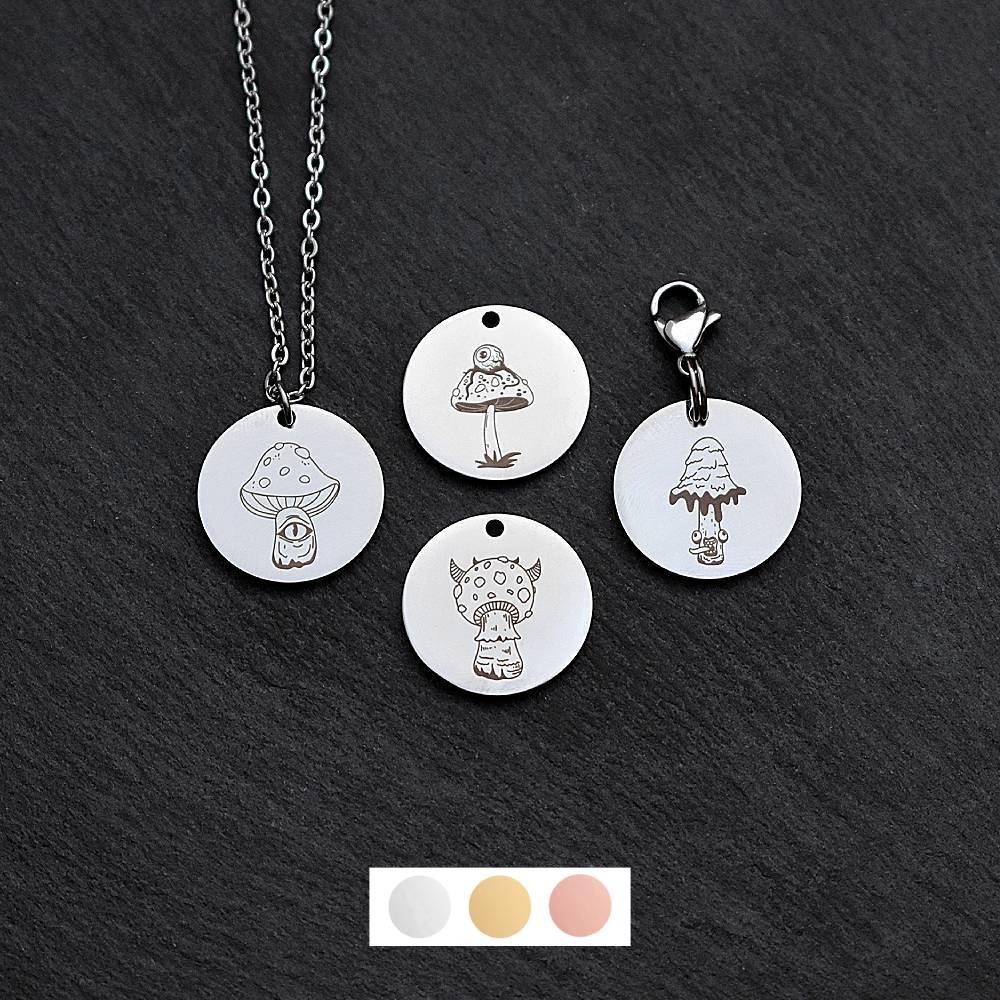 Four silver round disc pendants on a black slate background showing four different creepy mushroom toadstool designs. One has a silver necklace attached by a jump ring and another has a lobster clasp and split ring attached to it