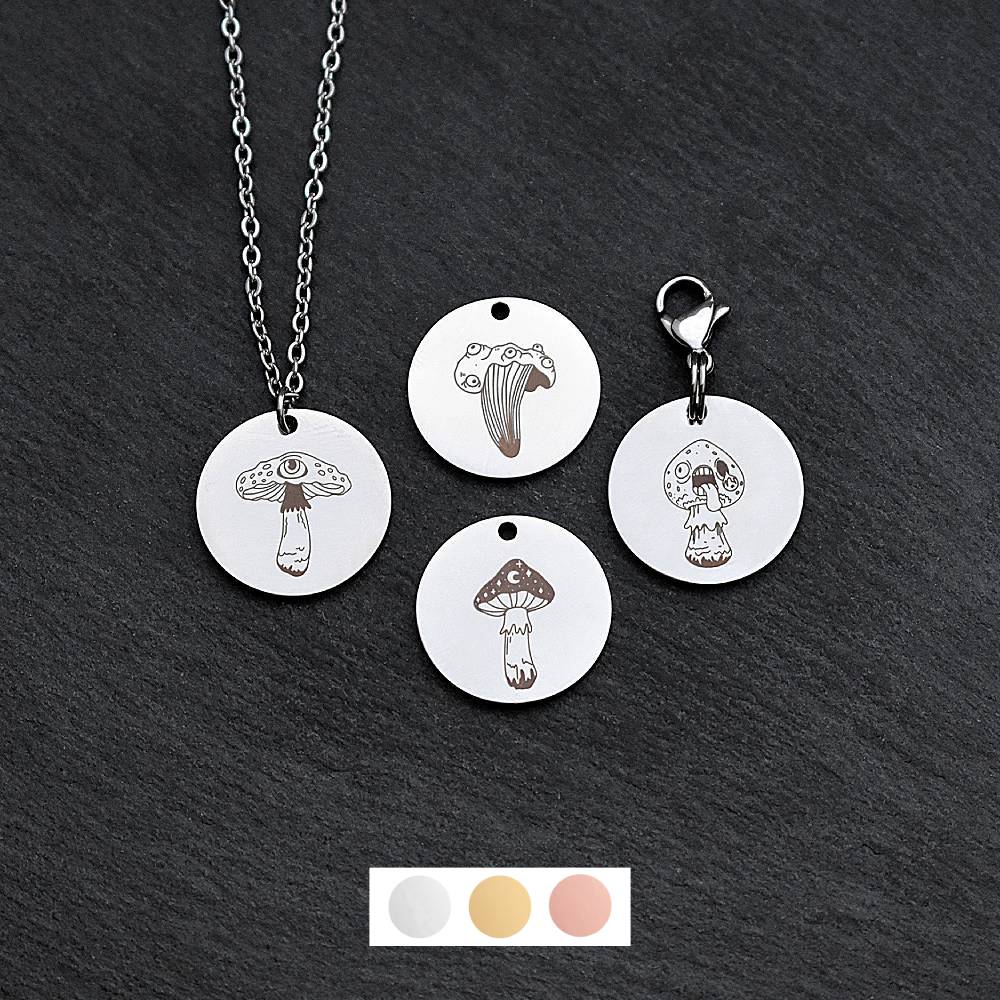 Four silver round disc pendants on a black slate background showing four different creepy mushroom toadstool designs. One has a silver necklace attached by a jump ring and another has a lobster clasp and split ring attached to it