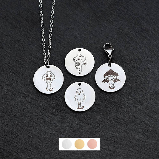 Four silver round disc pendants on a black slate background showing four different creepy mushroom toadstool designs. One has a silver necklace attached by a jump ring and another has a lobster clasp and split ring attached to it