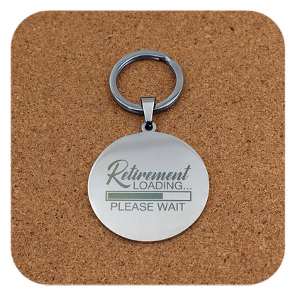 Silver keychain with 'Retirement Loading... Please Wait' text on a cork coaster