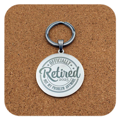 Silver keychain with 'Officially Retired 2025 Not My Problem Anymore' text on a cork background