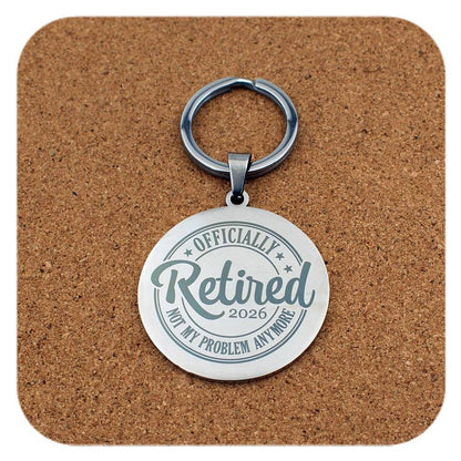Keychain with 'Officially Retired 2026 Not My Problem Anymore' text on a cork background