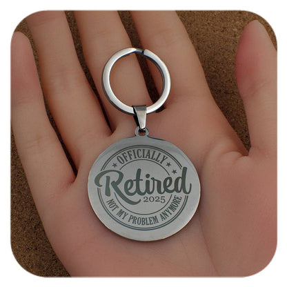 Silver keychain with 'Officially Retired 2025' text held in a hand.