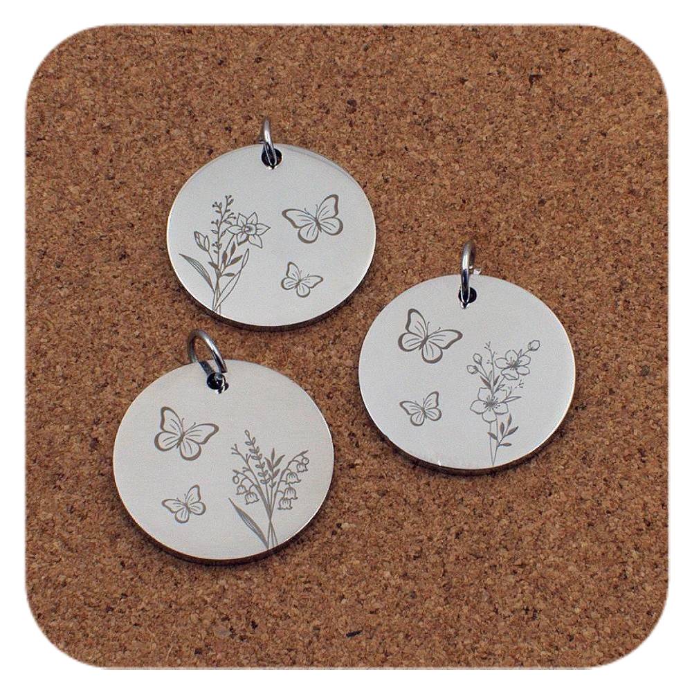 Three silver pendants with butterfly and floral designs on a cork background