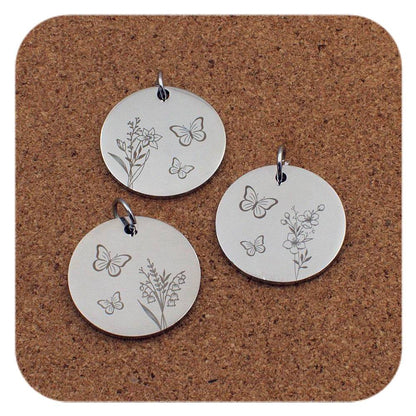 Three silver pendants with butterfly and floral designs on a cork background
