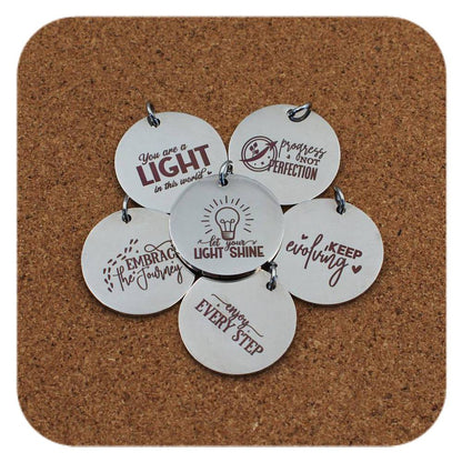 Silver pendants with different Daily Motivation designs on cork background