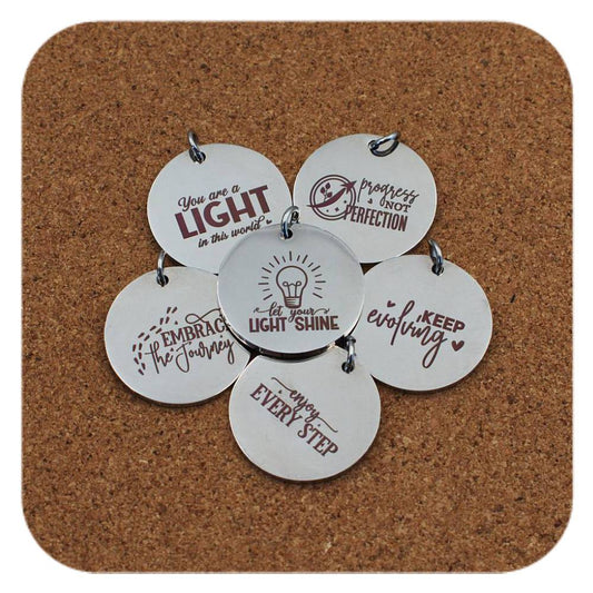Silver pendants with different Daily Motivation designs on cork background
