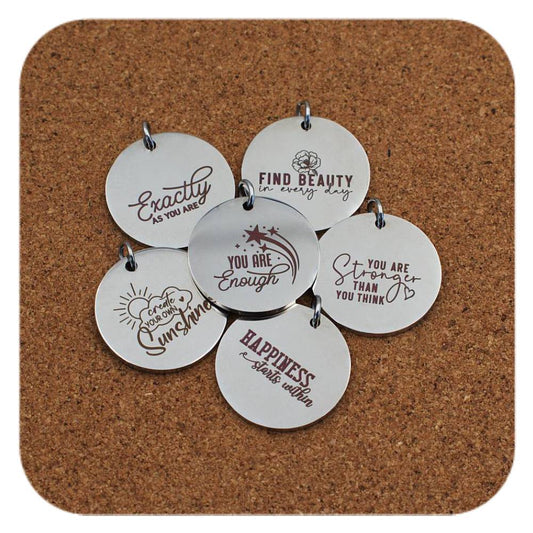 Silver pendants with different Uplifting Quote designs on cork background
