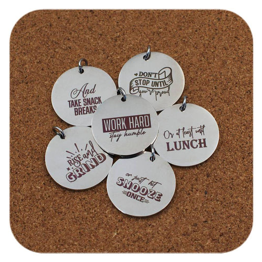 Silver pendants with different Laugh & Inspire designs on cork background